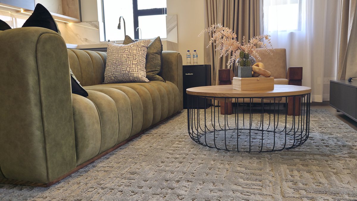Olive-green channelled sofa beside a round coffee table and textured rug.