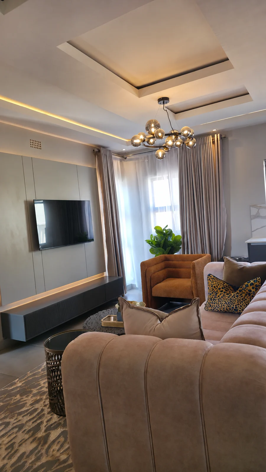 Esfog interior: living room with a wall-mounted television, upholstered seating and full-height curtains.
