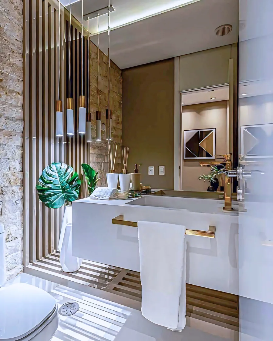 Bathroom vanity with gold fittings, a large mirror, vertical wall slats and suspended pendant lights.