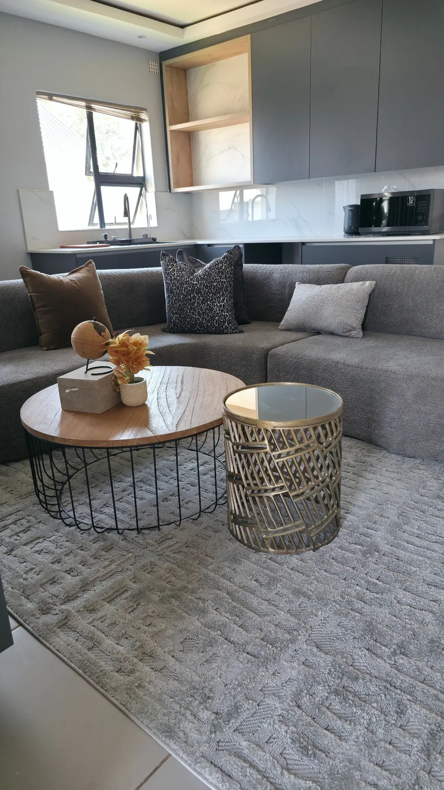 Esfog Lodge, Kadoma: lounge with grey seating, round tables and an adjoining kitchenette