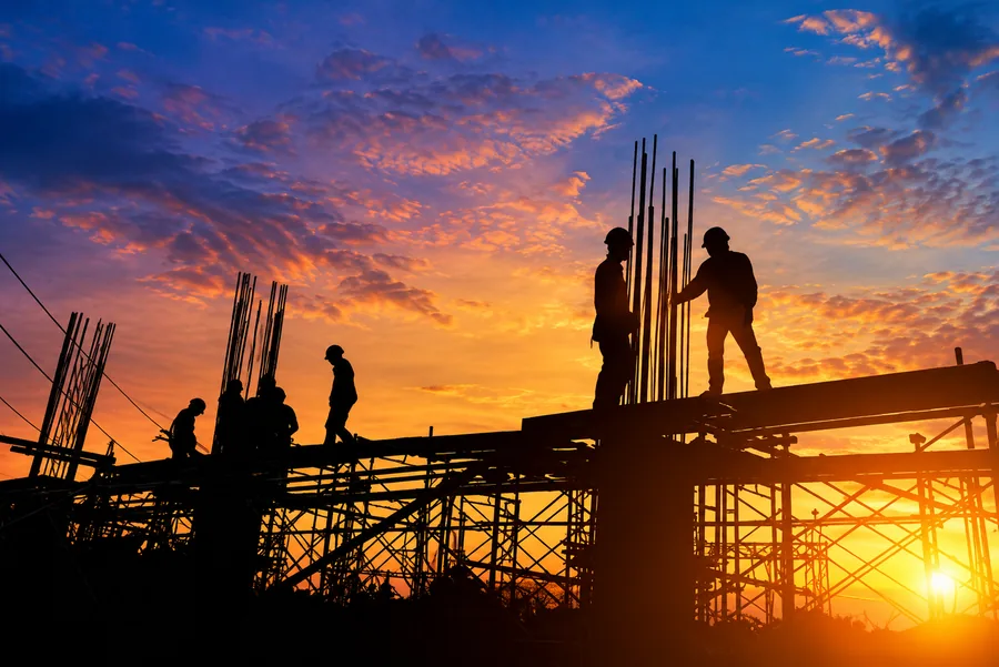 Silhouetted construction workers beside reinforcing steel and formwork at sunset