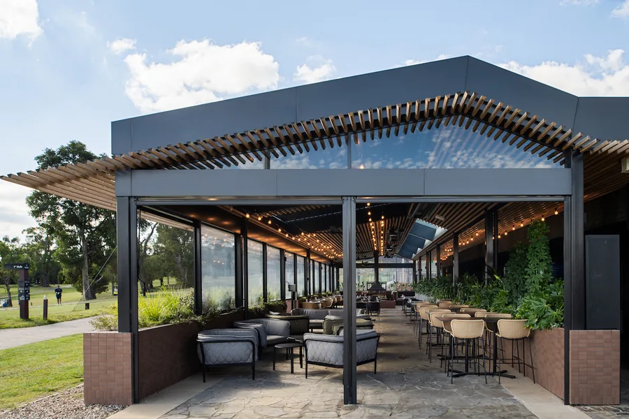 Open-sided restaurant pavilion with dining tables, timber ceiling and landscaped surroundings